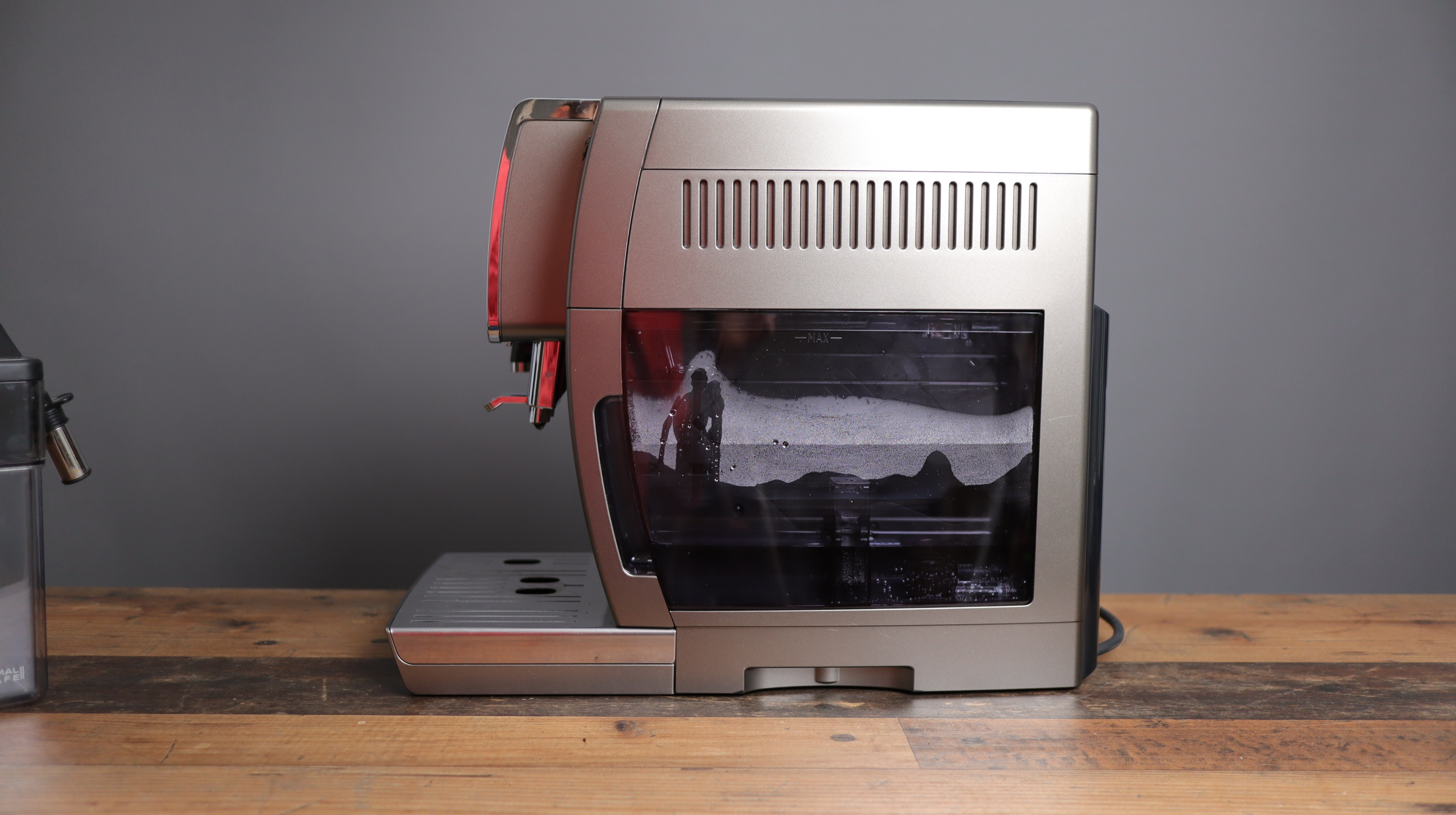 Delonghi Dinamica Plus shown from the right side, with exposed water tank.