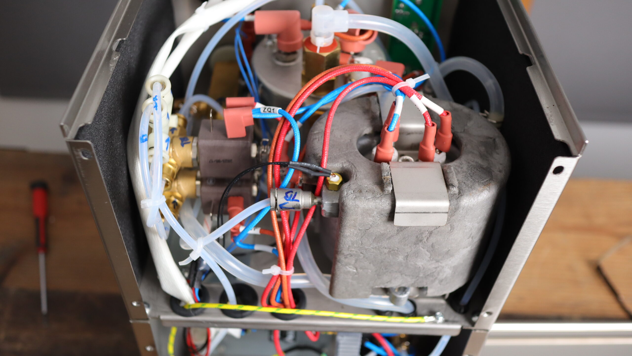 View of the inside of the MiiCoffee Apex, with the stainless steel brew boiler in the background, water circuits on the left, and thermoblock in the foreground